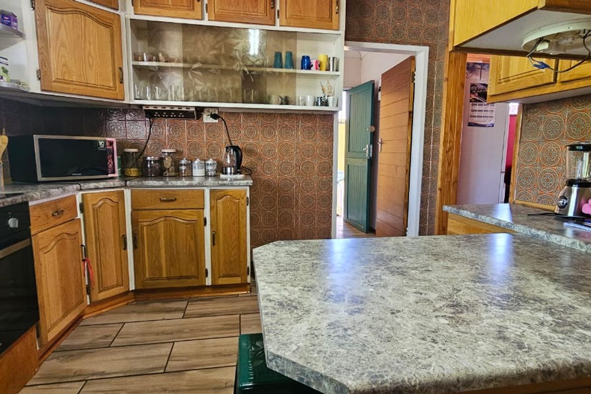 A dated kitchen featuring wood-look cabinetry, patterned wall tiles, and laminate countertops with an integrated oven and hob.