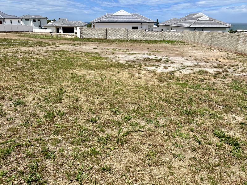 A vacant residential plot featuring a perimeter boundary wall, situated in a developed neighborhood with nearby coastal views.