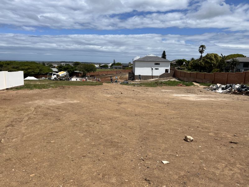 A wide-angle view of a vacant residential plot under development, featuring perimeter brick walls and surrounding neighborhood views.
