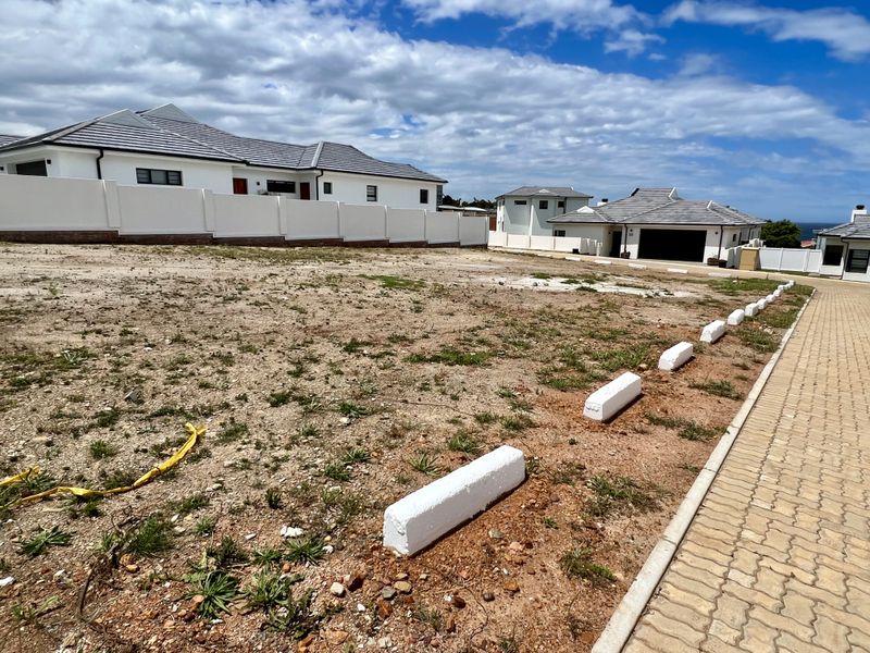 A vacant residential plot featuring a paved driveway, concrete boundary wall, and established parking curbs, situated in a developed neighborhood.
