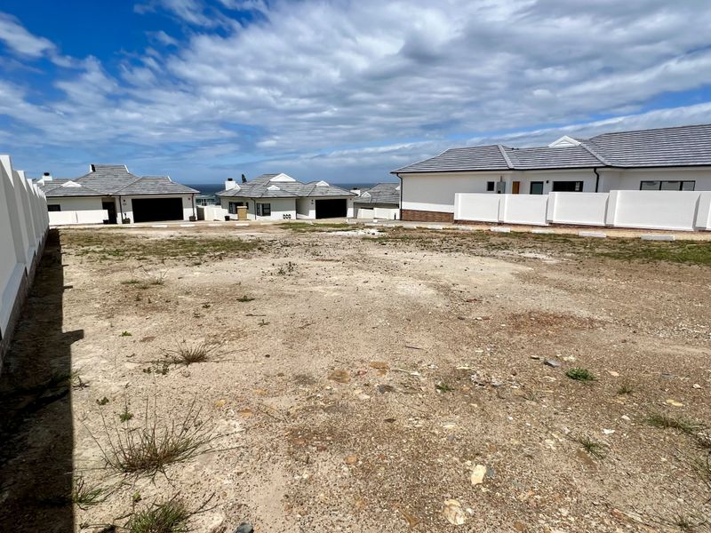 A vacant residential plot of land situated within a developed estate, featuring boundary walls and surrounding modern residential properties.