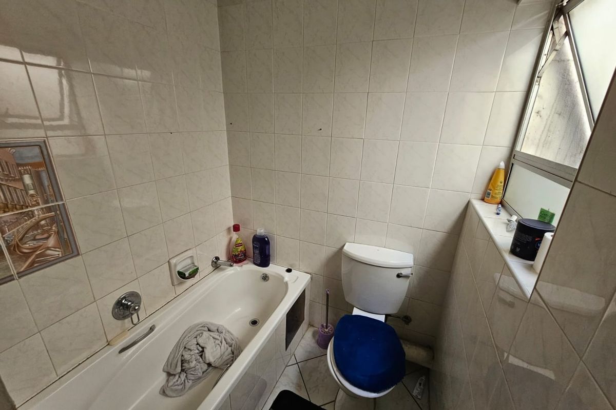A compact bathroom featuring a standard bathtub, toilet, and full-height wall tiling, requiring cosmetic updates to modernize the space.