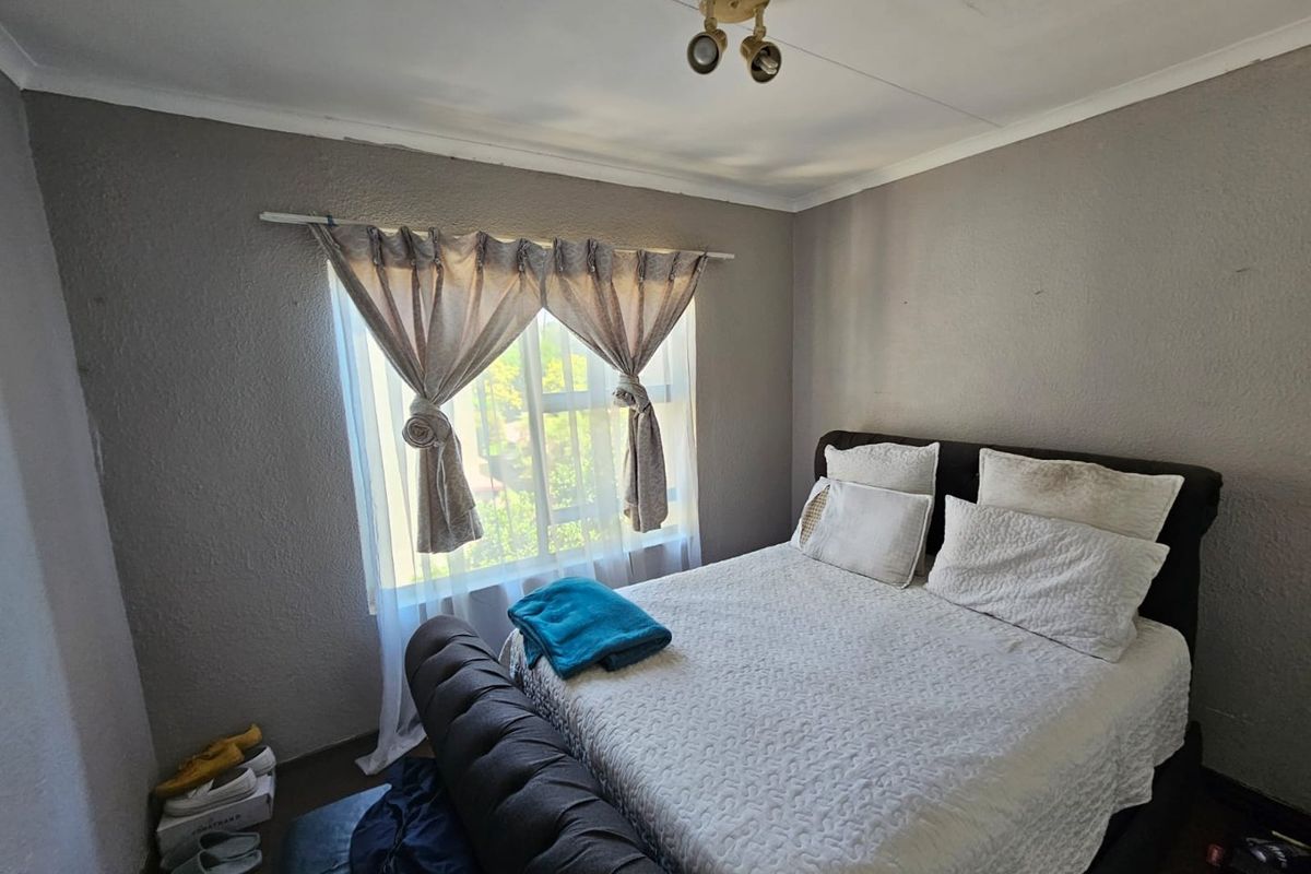 A bedroom featuring a window with curtain rod and ceiling mounted lighting. The room shows signs of wear on the walls and ceiling.