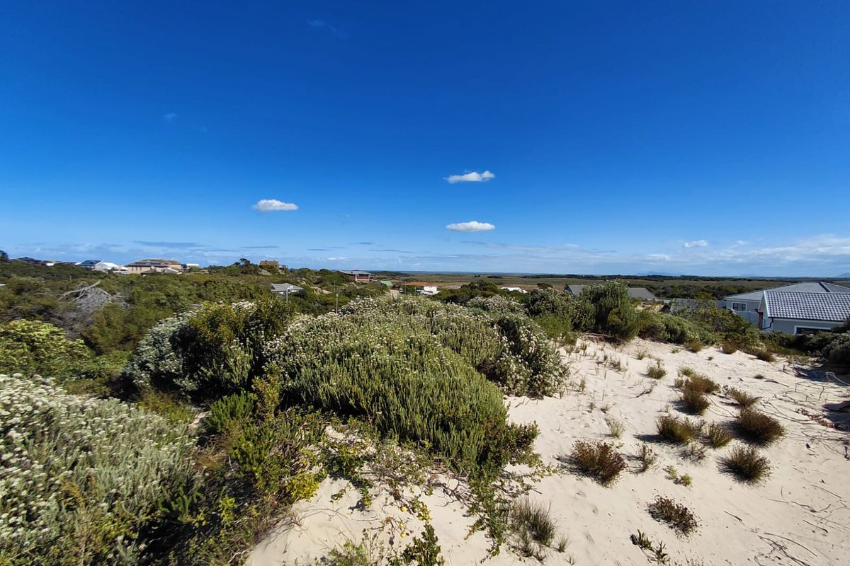 A wide-angle view of the vacant residential land featuring natural coastal vegetation and sandy terrain under a clear blue sky.