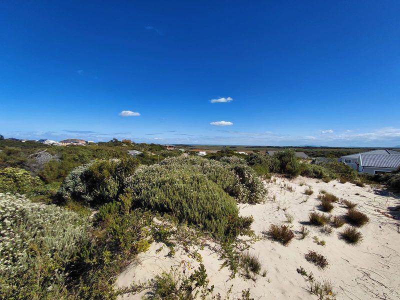 A wide-angle view of the vacant residential land featuring natural coastal vegetation and sandy terrain under a clear blue sky.