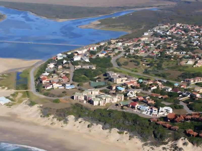 An aerial view of a coastal residential estate situated near an estuary and sandy beach.