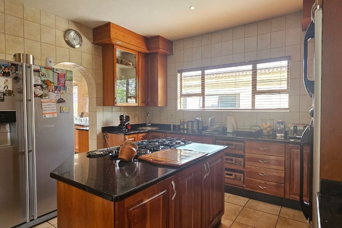 A functional kitchen featuring wooden cabinetry, a central island with a dark stone countertop, tiled backsplash, and a built-in gas hob.