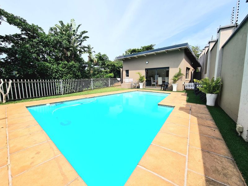 A well-maintained outdoor pool area featuring a tiled surround, artificial grass, and secure boundary walling with electric fencing.