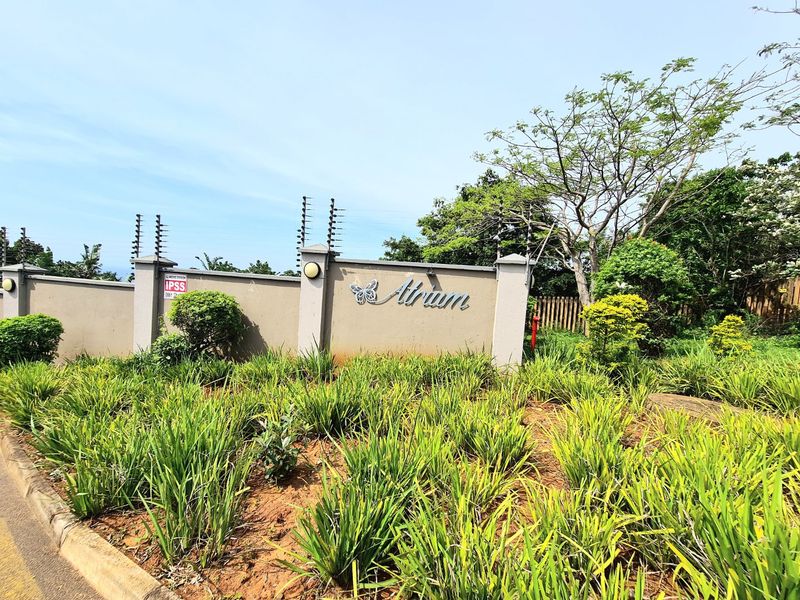 The front entrance of the Atrium complex, featuring a secure perimeter wall with electric fencing and well-maintained garden landscaping.
