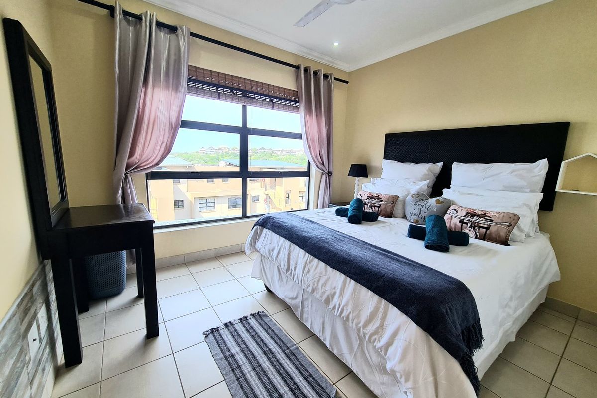 A well-lit bedroom featuring tiled flooring, a ceiling fan, and a large window providing natural light and exterior views.