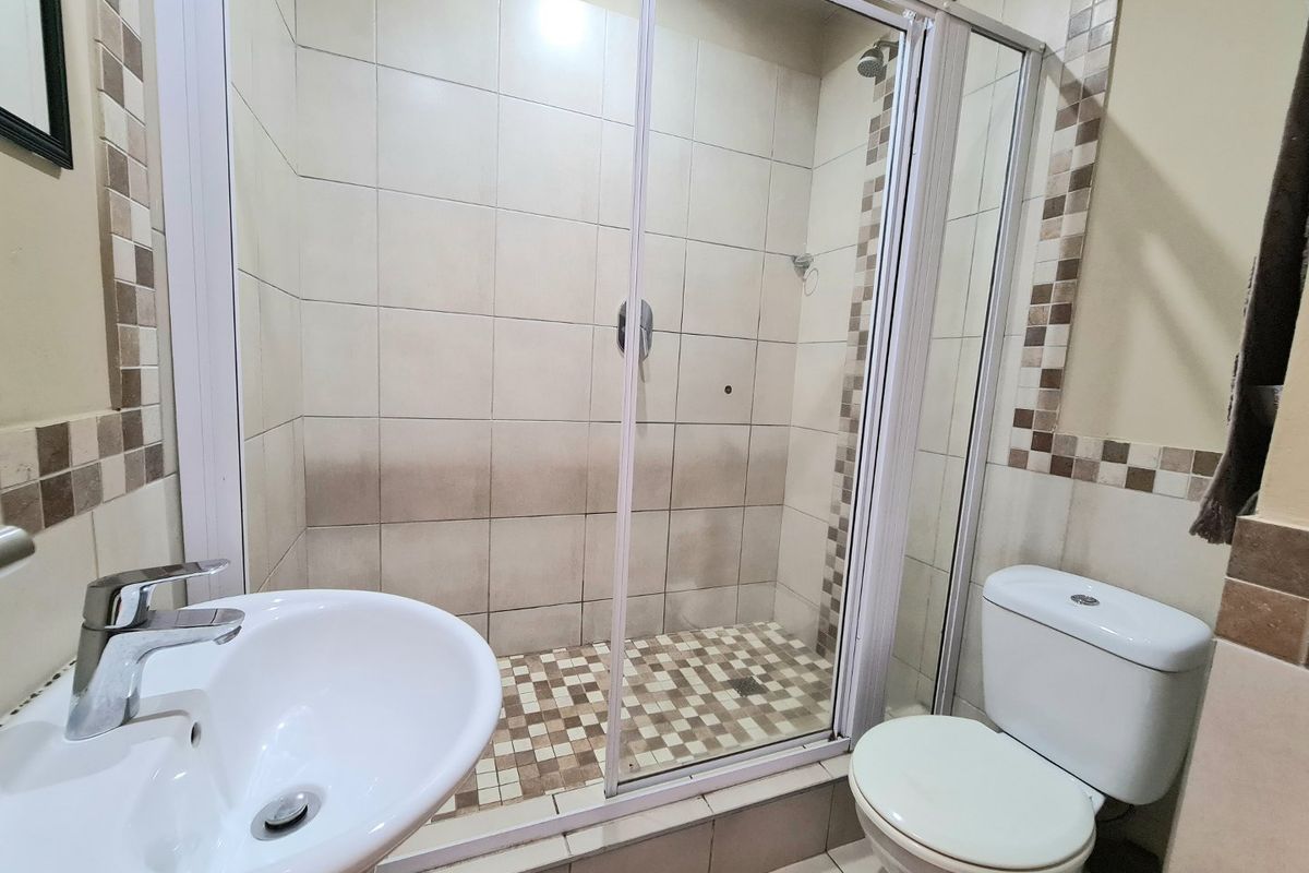 A functional bathroom featuring a glass-enclosed shower, pedestal basin, and standard toilet with neutral tiled finishes.