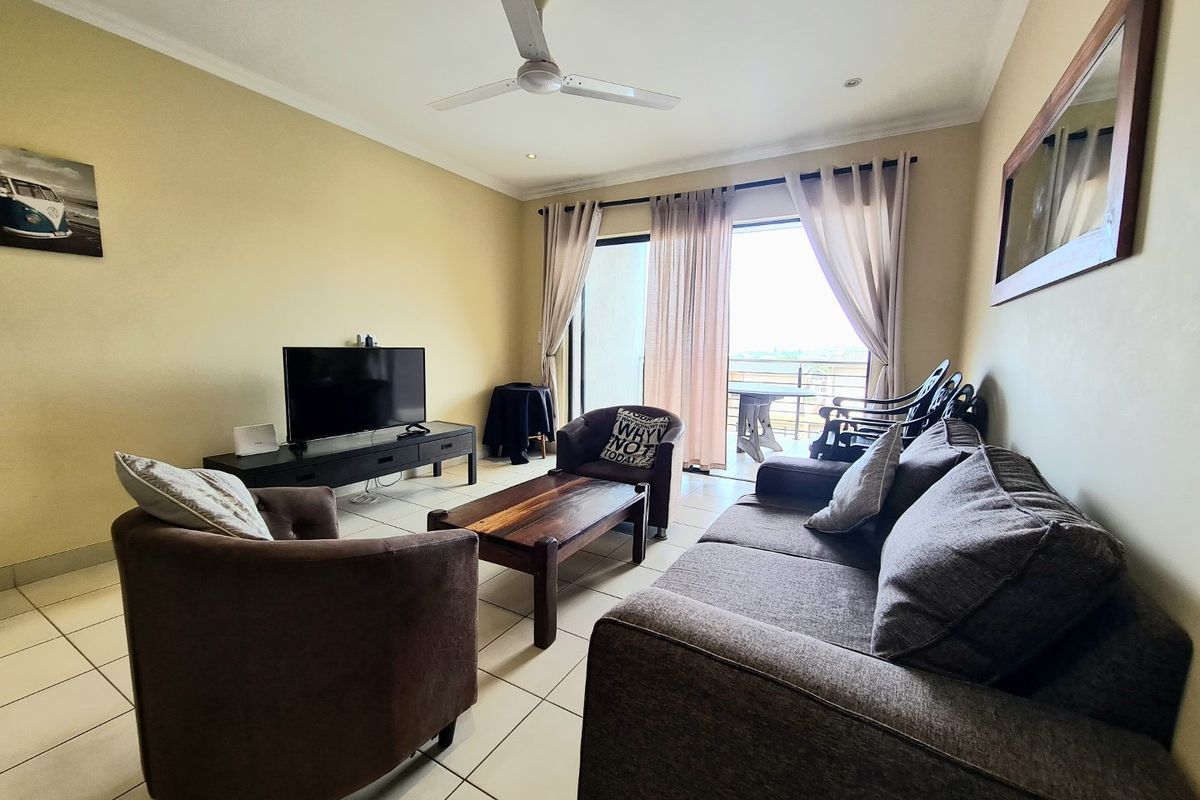 A comfortable living room featuring tiled flooring, a ceiling fan, and large sliding glass doors that provide access to an outdoor balcony area.