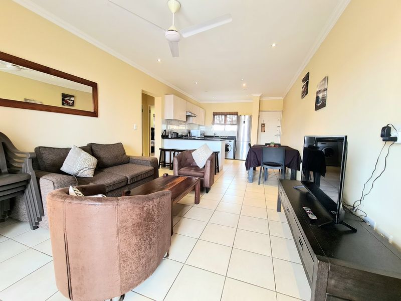Open-plan living and dining area featuring tiled flooring, a breakfast bar, and a functional kitchen with built-in cabinetry and an extractor fan.