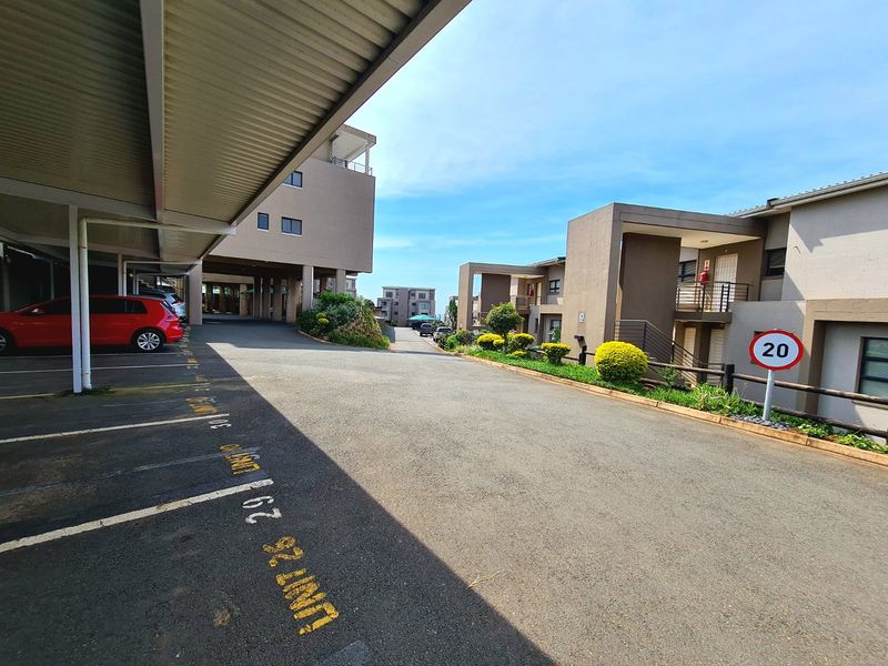 A view of the complex driveway featuring covered parking bays, paved access roads, and landscaped garden areas within the residential estate.