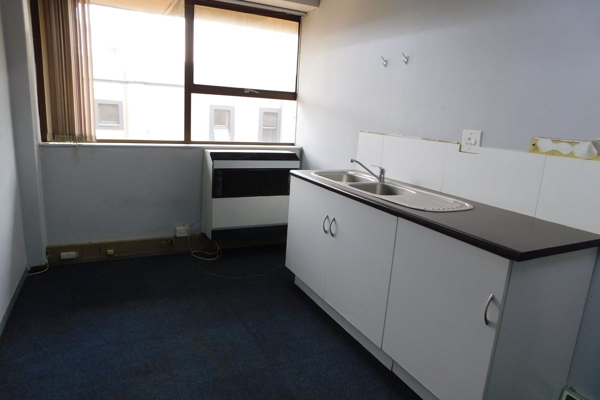 A small office kitchenette featuring a stainless steel sink, built-in base cabinetry, and a window with vertical blinds.