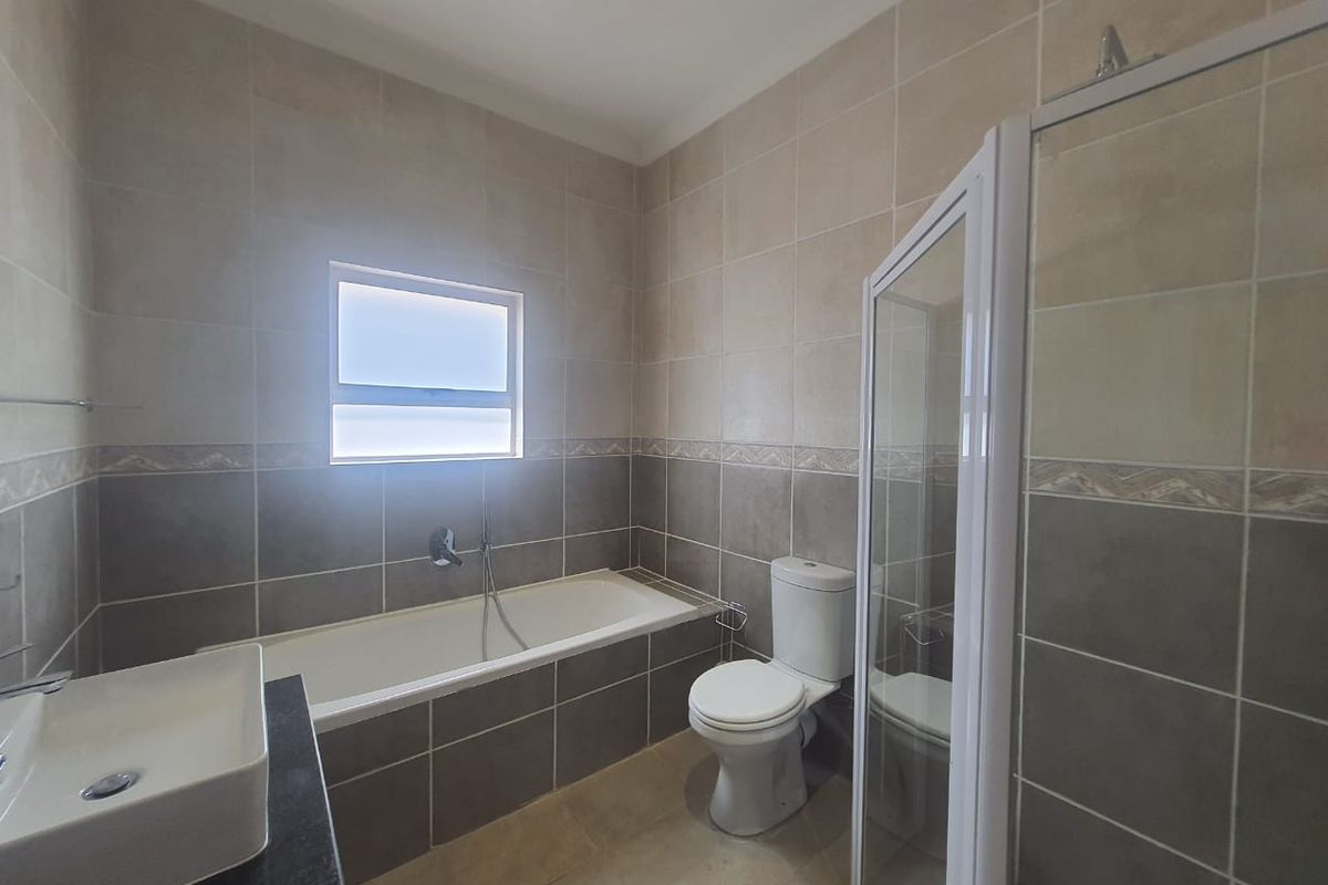 A modern bathroom featuring a built-in bathtub, a separate glass-enclosed shower, a toilet, and a vanity basin with tiled walls.