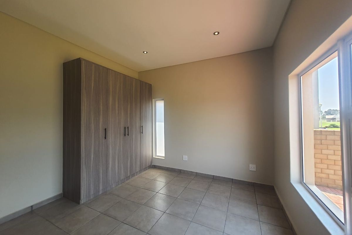 A bright, empty bedroom featuring neutral tiled flooring, recessed ceiling lighting, and modern built-in wooden cabinetry.