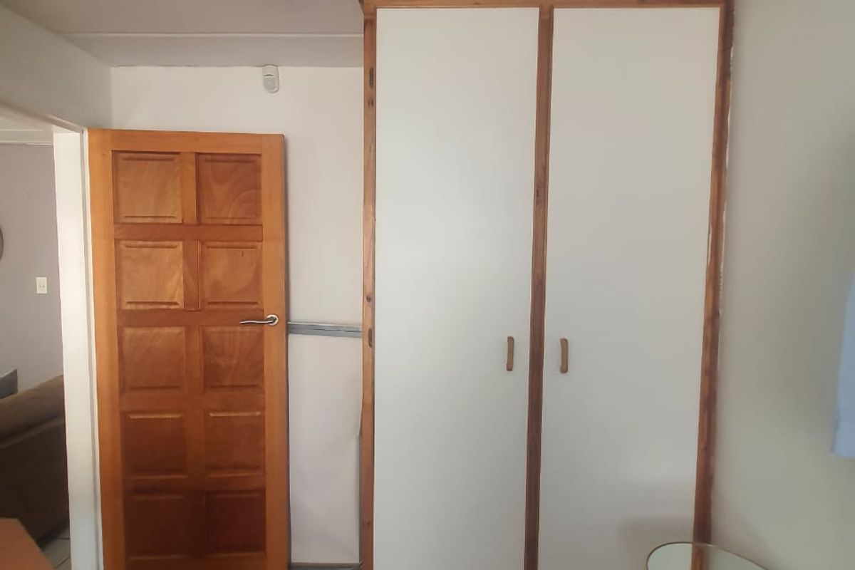 A bedroom interior featuring built-in wooden-framed cupboards and a solid timber panel door with laminate flooring.