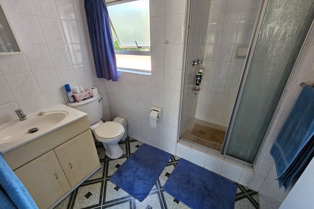 A functional bathroom featuring a vanity cabinet, toilet, and a glass-enclosed shower with tiled walls and patterned flooring.