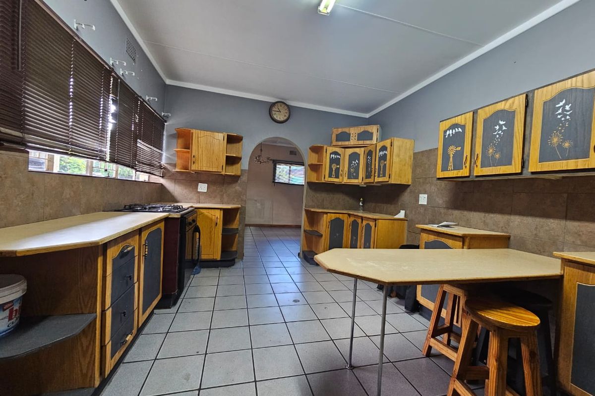 A dated kitchen featuring wooden cabinetry, laminate countertops, a gas hob, and tiled flooring, offering potential for a modern renovation.