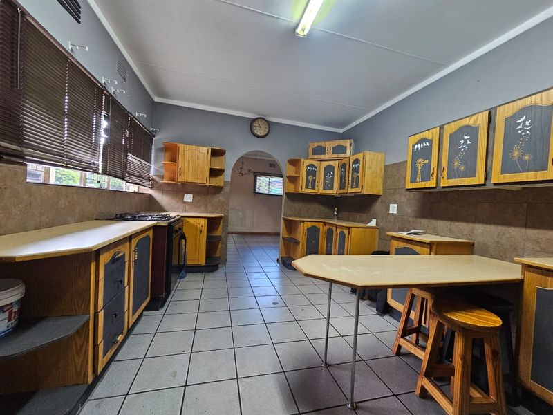 A dated kitchen featuring wooden cabinetry, laminate countertops, a gas hob, and tiled flooring, offering potential for a modern renovation.