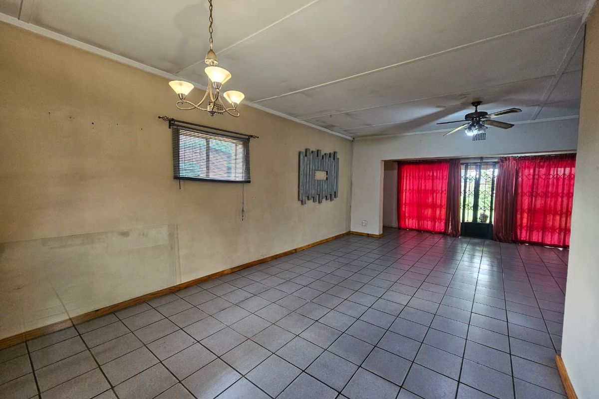 Spacious living area featuring tiled flooring, a ceiling fan, and a chandelier, offering a blank canvas for potential interior updates.