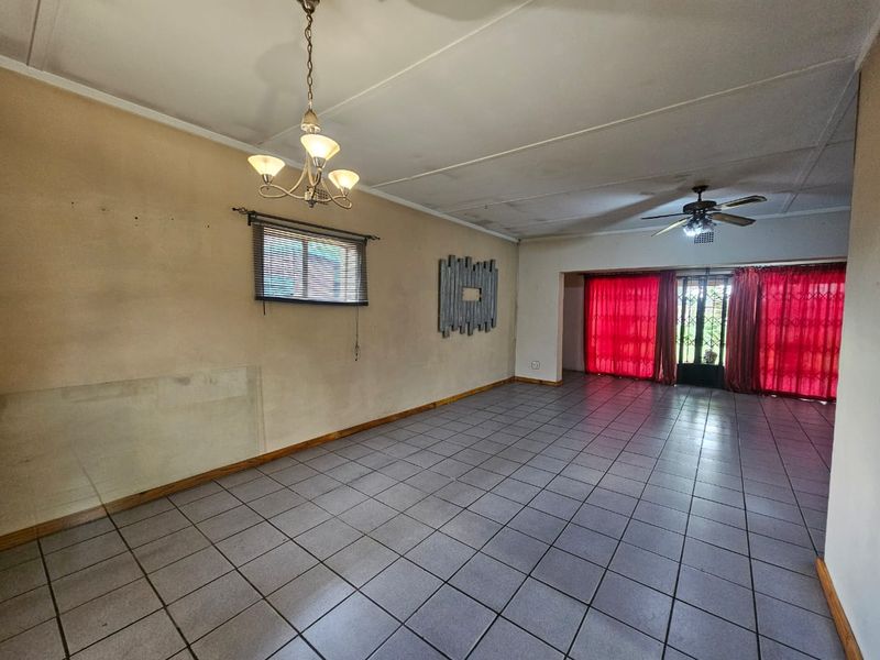 Spacious living area featuring tiled flooring, a ceiling fan, and a chandelier, offering a blank canvas for potential interior updates.