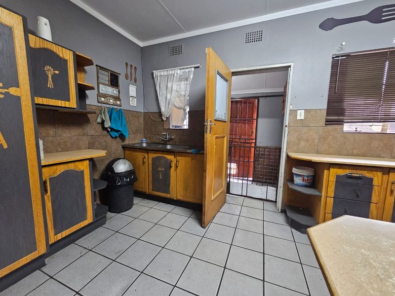 A functional kitchen featuring built-in wooden cabinetry, tiled flooring, and a tiled splashback, with direct access to an exterior security gate.