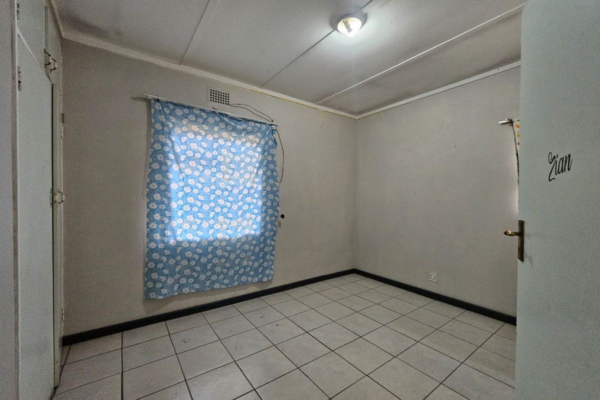 An empty bedroom featuring tiled flooring, a built-in cupboard, and neutral wall finishes, offering a blank canvas for personalization.