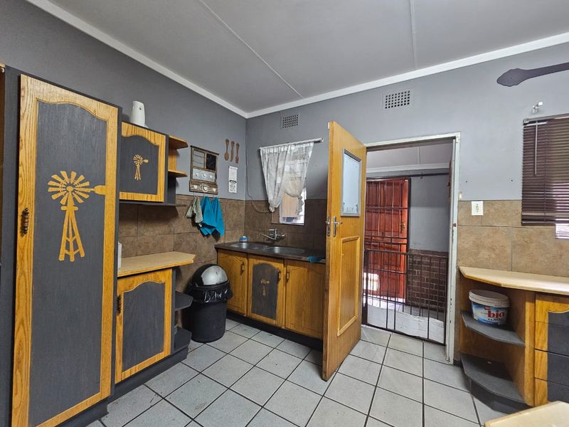 A functional kitchen area featuring built-in wooden cabinetry, tiled flooring, and a double sink, with direct access to an exterior security gate.