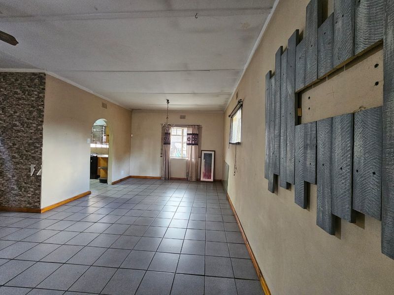 Spacious living area featuring tiled flooring, a stone-clad feature wall, and an archway leading to the kitchen. The room is vacant and ready for staging.