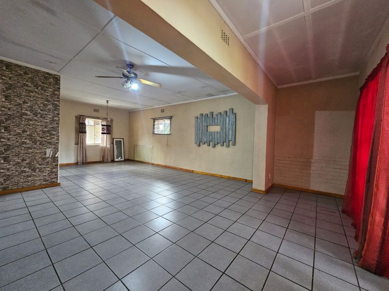 A spacious, open-plan living area featuring tiled flooring, a stone feature wall, and a ceiling fan, offering a blank canvas for interior design.