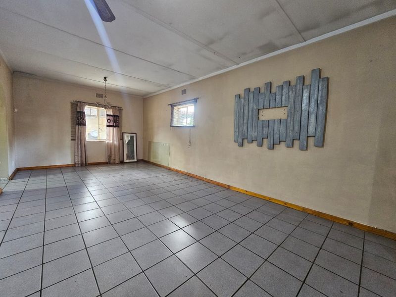 A spacious, empty living area featuring tiled flooring, a ceiling fan, and neutral wall finishes, offering a blank canvas for potential renovation.