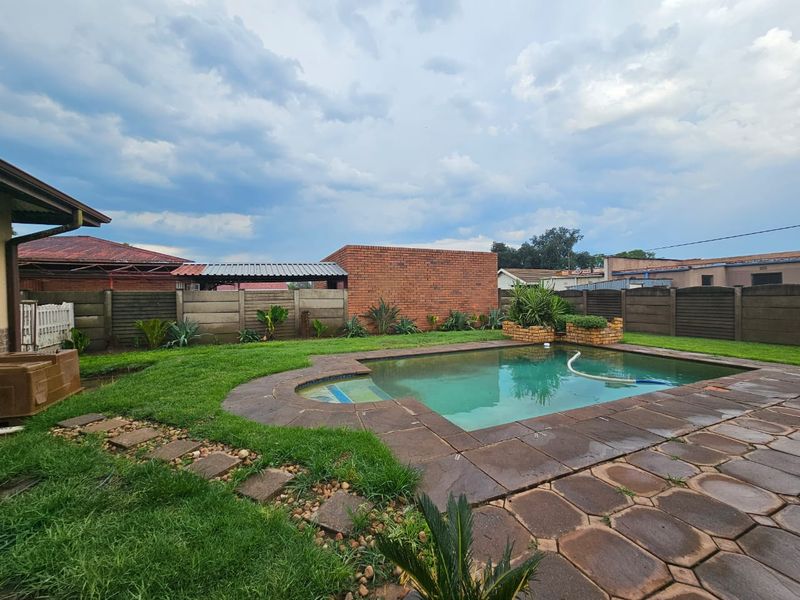Outdoor pool area featuring a swimming pool with paved surround, set within a garden enclosed by brick and precast concrete boundary walls.