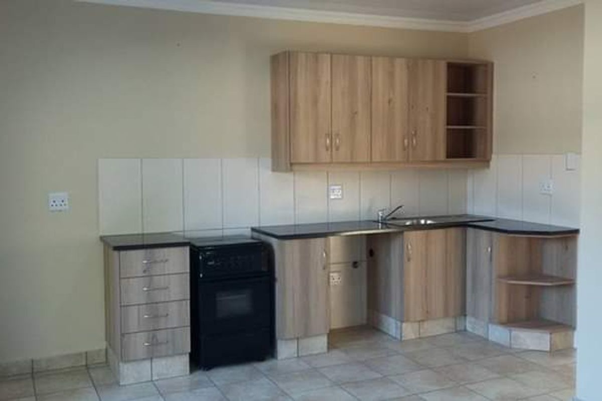 A functional kitchen featuring light wood-finish cabinetry, dark countertops, tiled splashbacks, and a built-in stove, offering a clean and practical workspace.