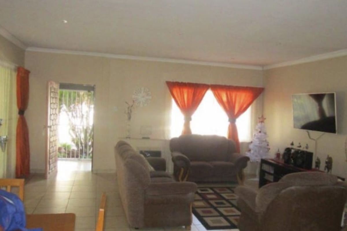 Spacious living room featuring tiled flooring, neutral wall tones, and direct access to an outdoor area through a security gate.