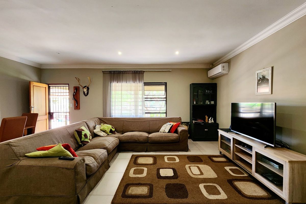 A spacious living room featuring tiled flooring, recessed downlighting, crown molding, and a wall-mounted air conditioning unit.