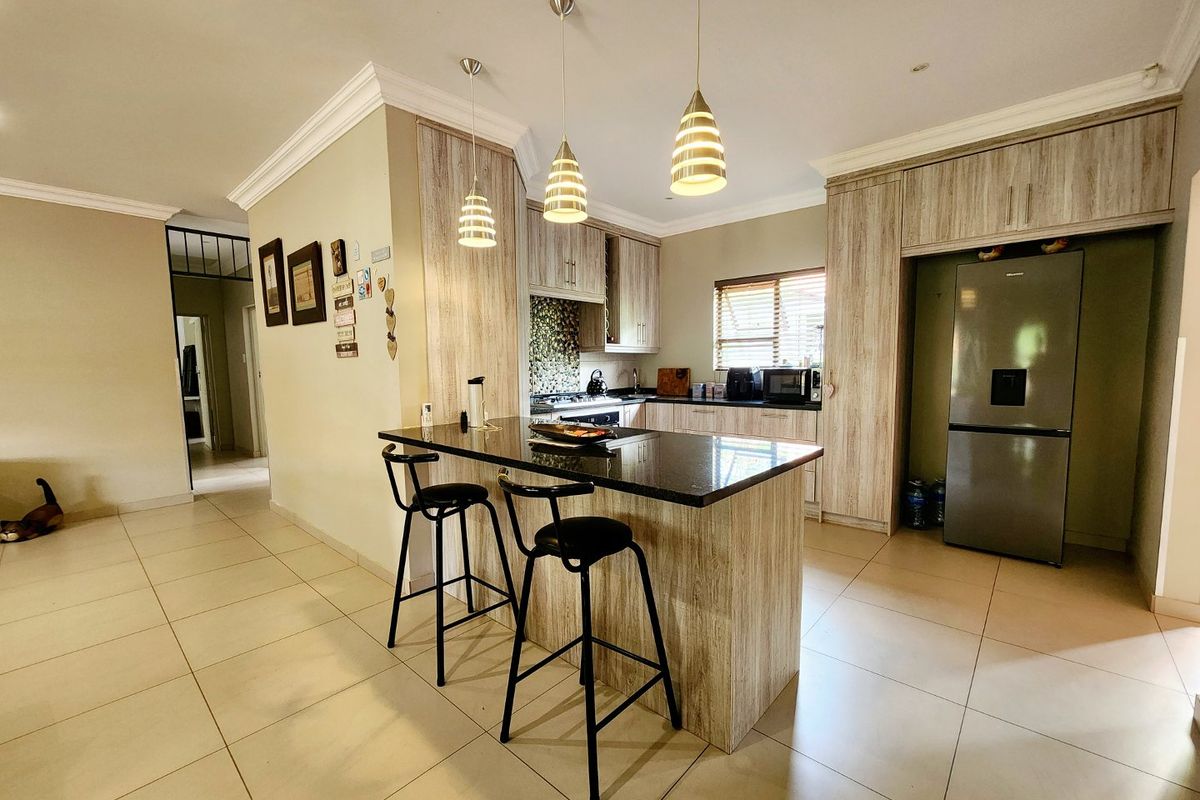 Modern kitchen featuring wood-grain cabinetry, a central breakfast island with stone countertop, tiled flooring, and integrated lighting.