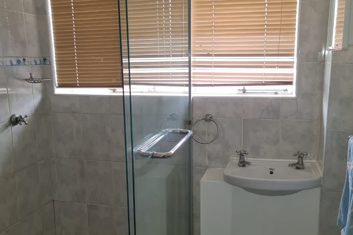 A functional bathroom featuring a glass-enclosed shower, a built-in vanity basin, and tiled walls with window blinds.