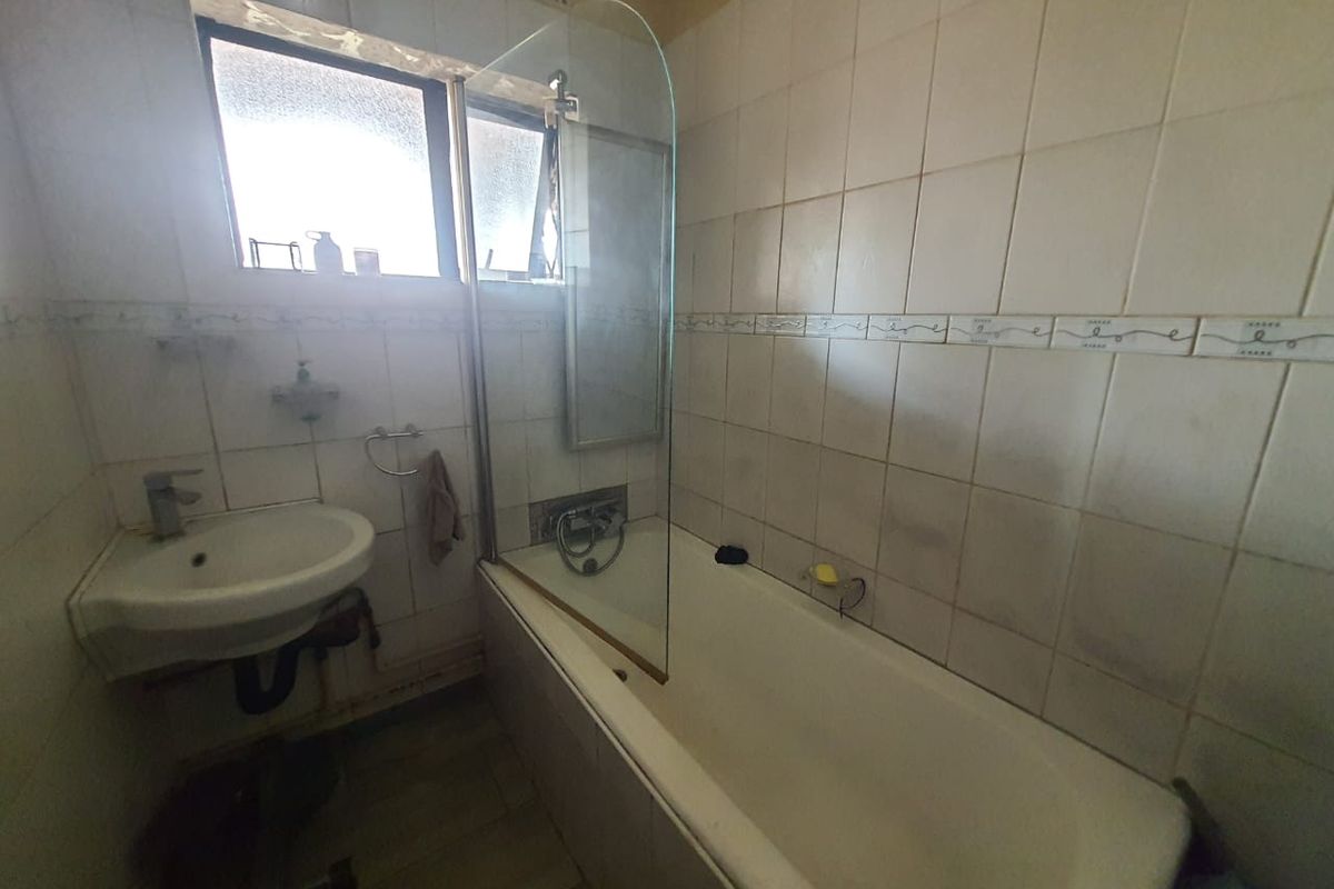 A dated bathroom featuring a built-in bathtub with a glass shower screen, a wall-mounted basin, and tiled walls.