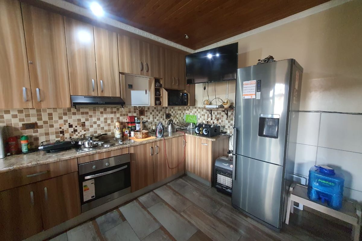 A functional kitchen featuring wood-look cabinetry, tiled backsplash, built-in oven, and extractor fan, with a tiled floor and wood-paneled ceiling.