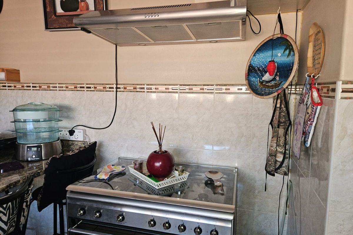 A kitchen cooking area featuring a stainless steel freestanding stove, extractor fan, and tiled splashback.