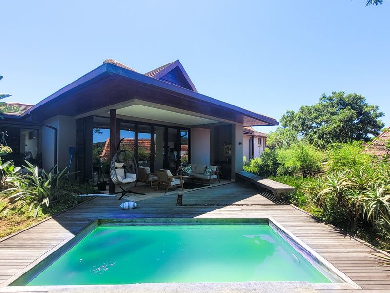 Outdoor pool area featuring timber decking, a covered patio space, and direct access to the home through large sliding glass doors.