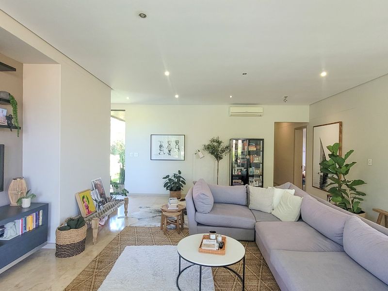A bright and spacious living room featuring tiled flooring, recessed downlighting, and a wall-mounted air conditioning unit.