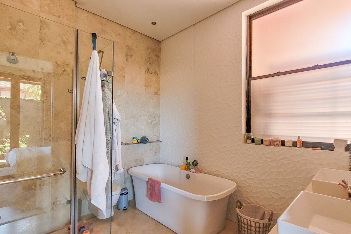Modern bathroom featuring a freestanding bathtub, glass-enclosed shower, dual vanity sinks, and elegant travertine and textured wall tiling.