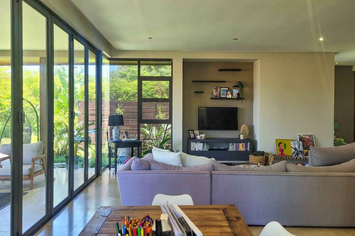 Spacious living room featuring large aluminium sliding doors that open to a garden patio, with a built-in media alcove and modern recessed lighting.