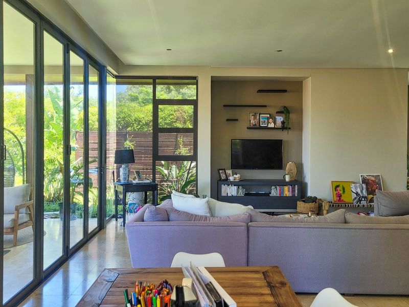 Spacious living room featuring large aluminium sliding doors that open to a garden patio, with a built-in media alcove and modern recessed lighting.