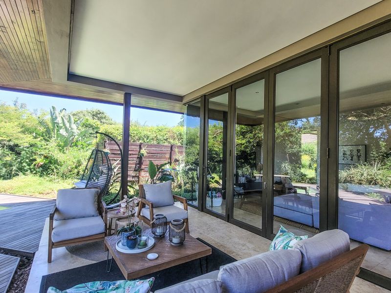 A covered patio featuring stone flooring and timber ceiling details, seamlessly connecting to the garden and swimming pool area through large sliding glass doors.