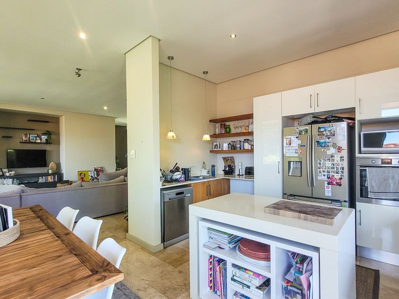 Open-plan living area featuring a modern kitchen with stone countertops, built-in appliances, and a central island, flowing into a comfortable lounge space.