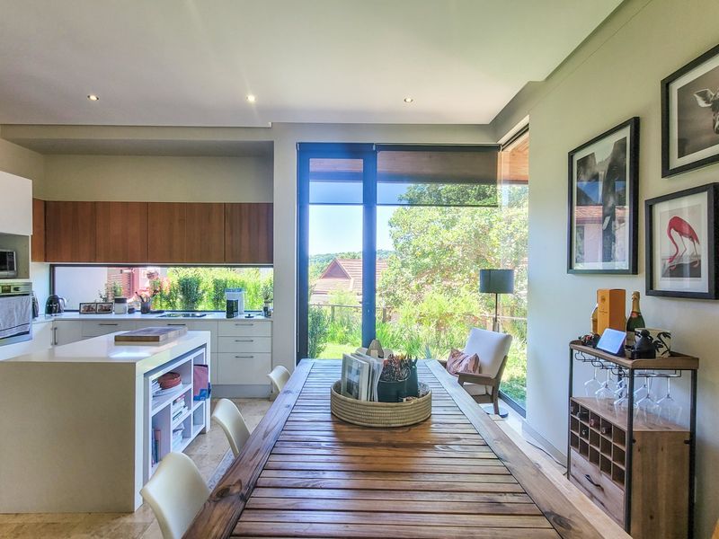 Modern open-plan kitchen and dining area featuring sleek cabinetry, a central island, and large glass doors providing seamless access to the garden.